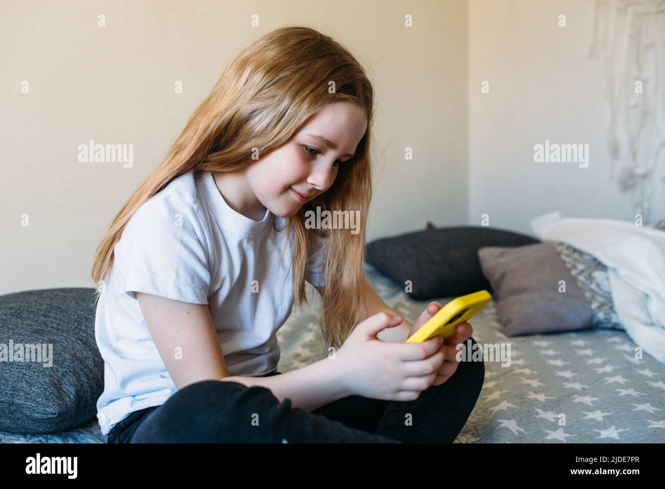 Girl child at home on the couch uses a smartphone Stock Photo