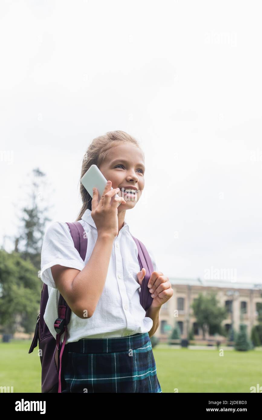 Smiling schoolchild with backpack talking on mobile phone outdoors Stock Photo