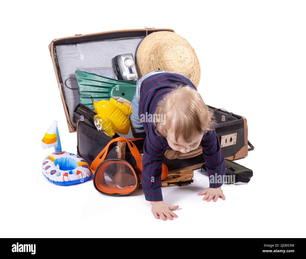 A little boy crawling from a suitcase with travel equipment, on white