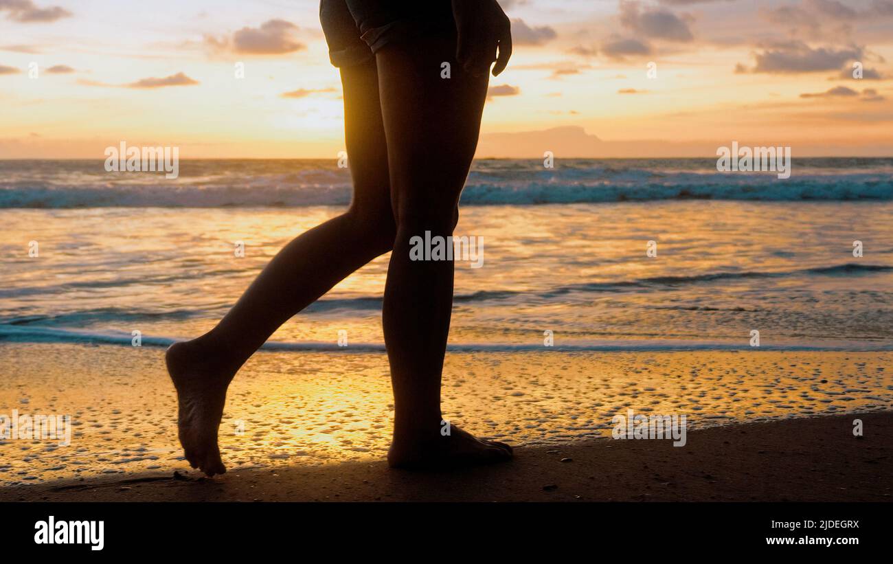 Young Woman Feet Walking Barefoot On Beach By Sea At Golden Sunset