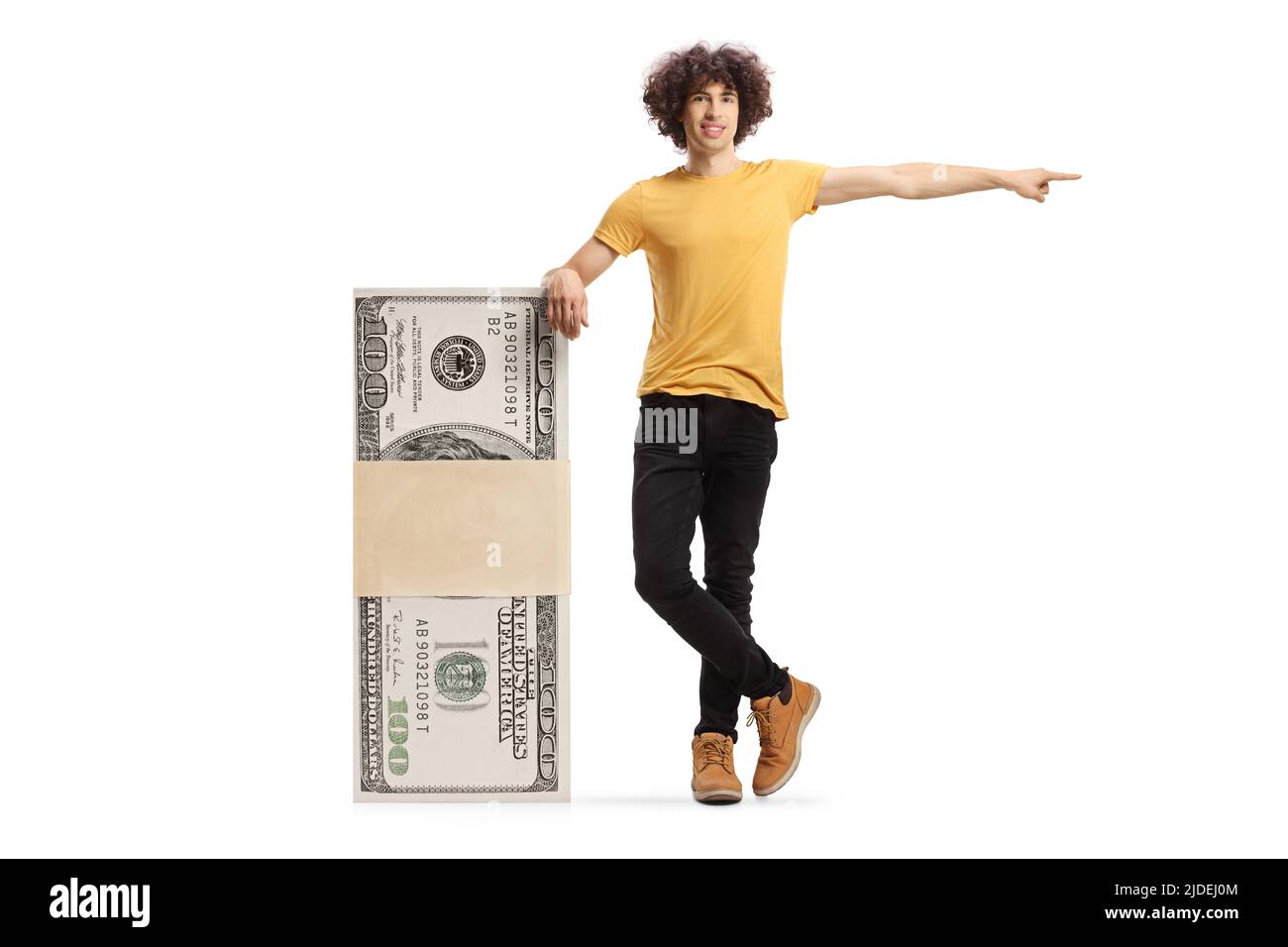 Young man leaning on a stack of money and pointing isolated on white background Stock Photo