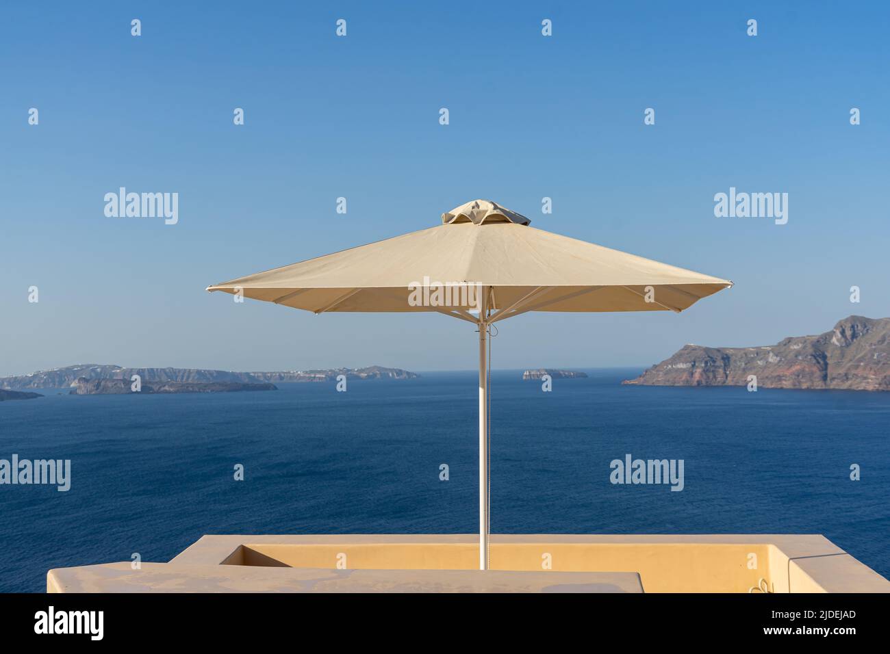 A single parasol on a rooftop patio in Oia divides the panoramic view of Santorini's caldera Stock Photo