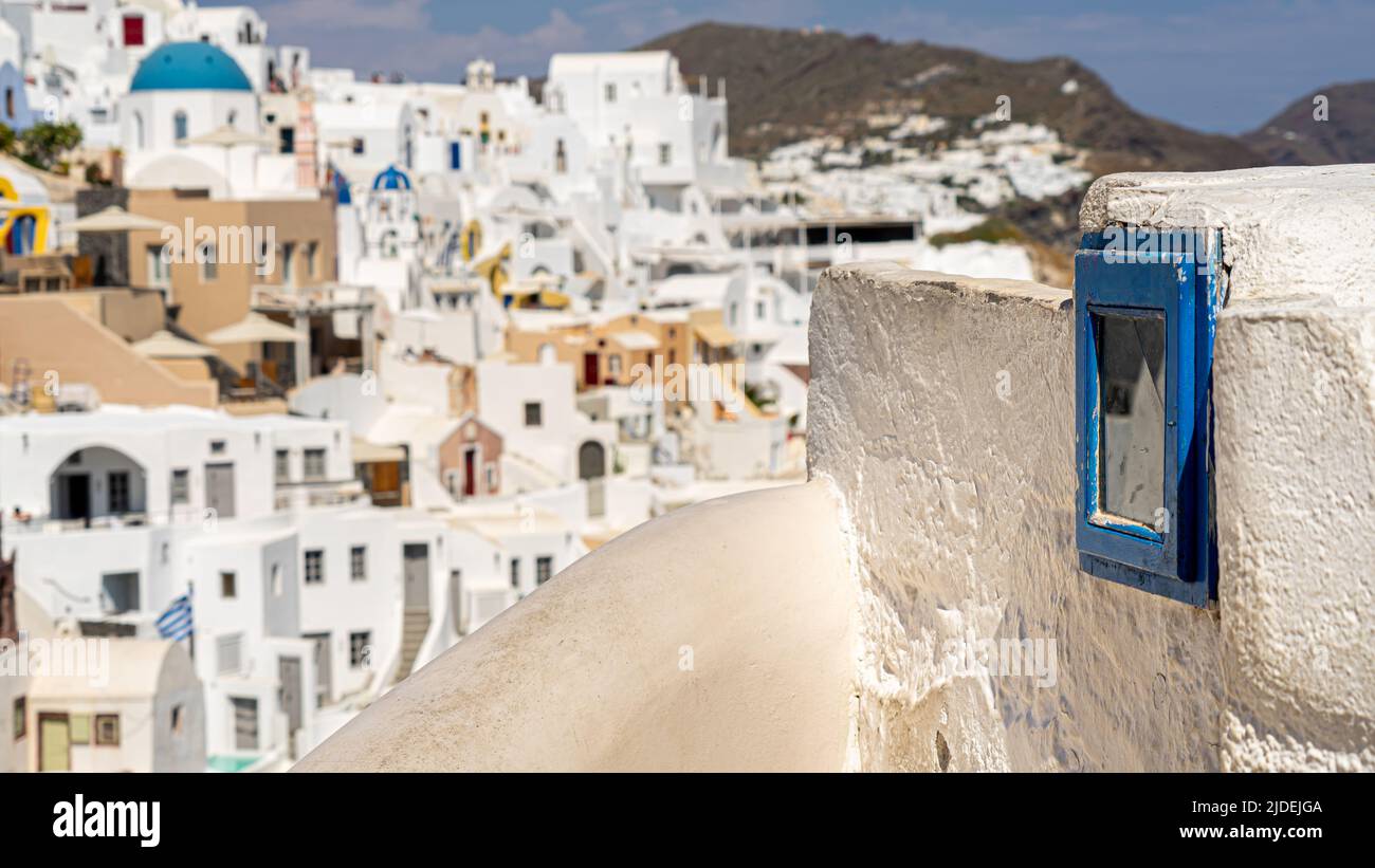 An old prayer niche in Oia with the town in the background in a panoramic shot with a shallow focus Stock Photo