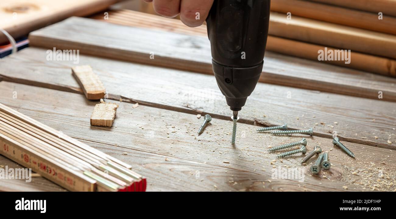 Screwdriver electric tool, male hand screw on wood.  Carpenter work bench table closeup view. DIY, home repair and fix. Stock Photo