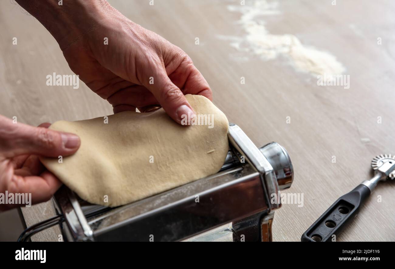 Fresh pasta maker machine. Dough homemade preparation. Male hand making dough phylo for pies and pastry, close up view Stock Photo