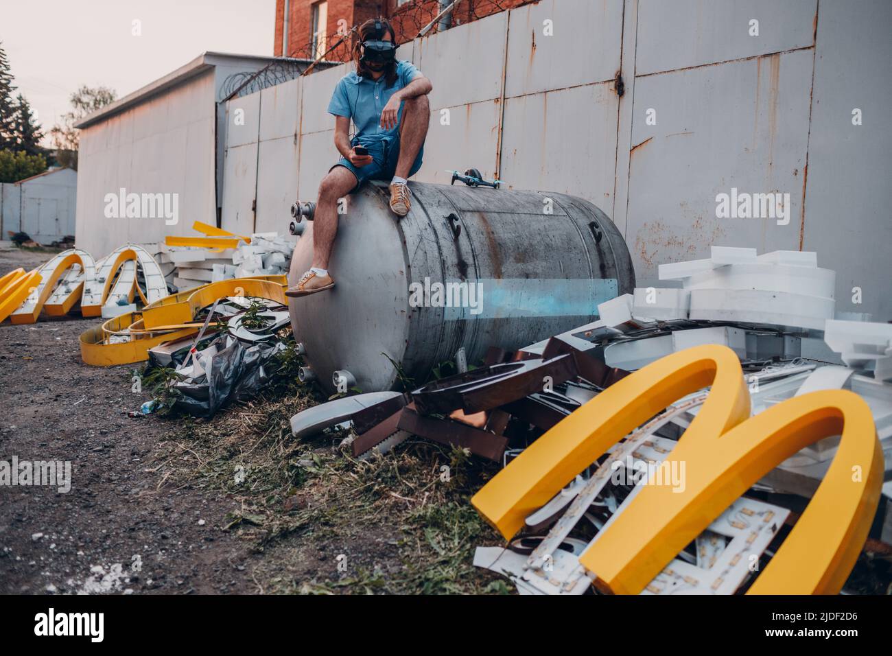 Moscow, Russia - 06.21.2022: Young man sitting on VR headset and McDonalds logo letter character M on dirty rubbish heap dump trash litter garbage. Fa Stock Photo