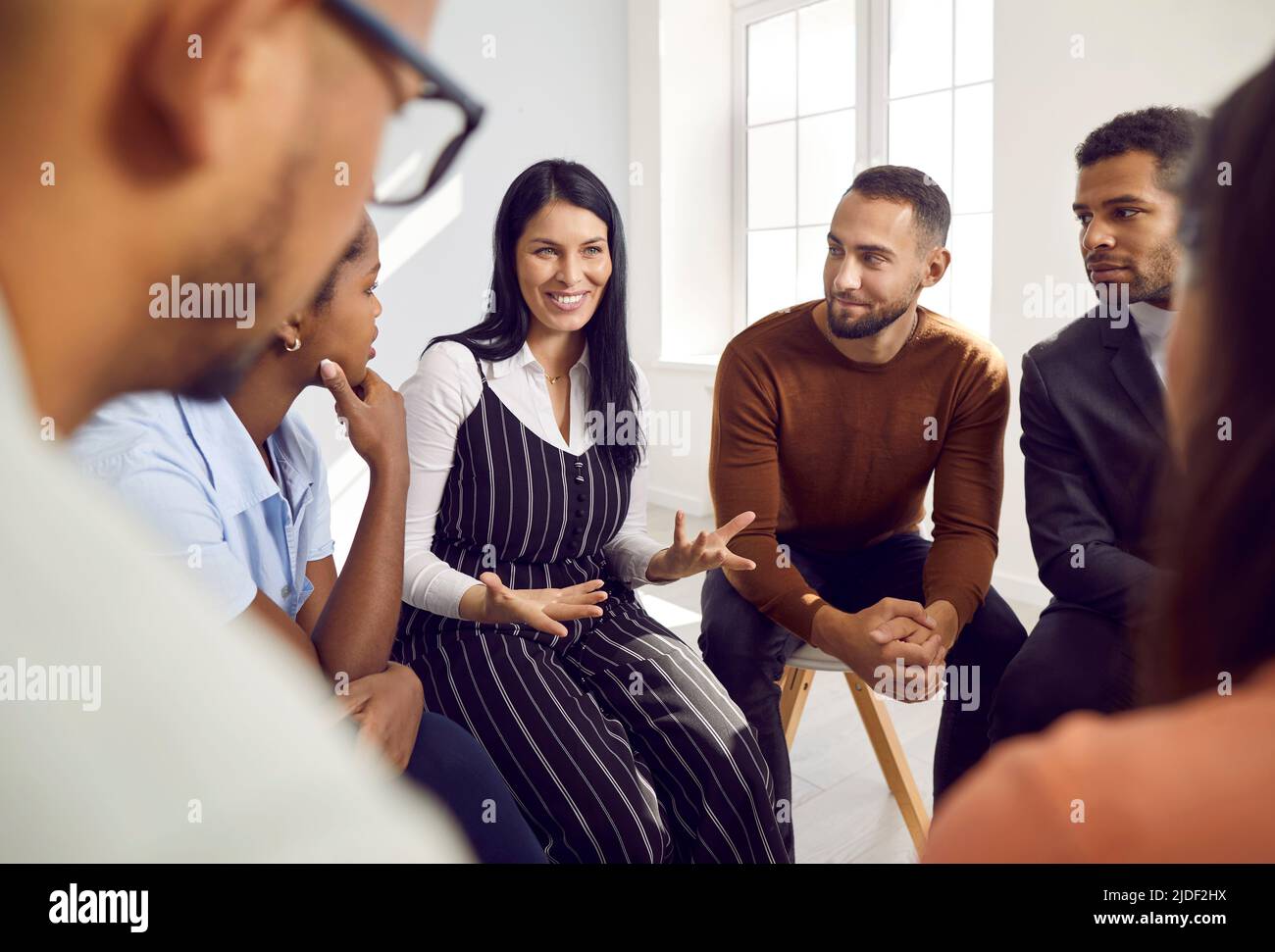 Young emotional woman tells about herself and her story to other people at support group meeting. Stock Photo