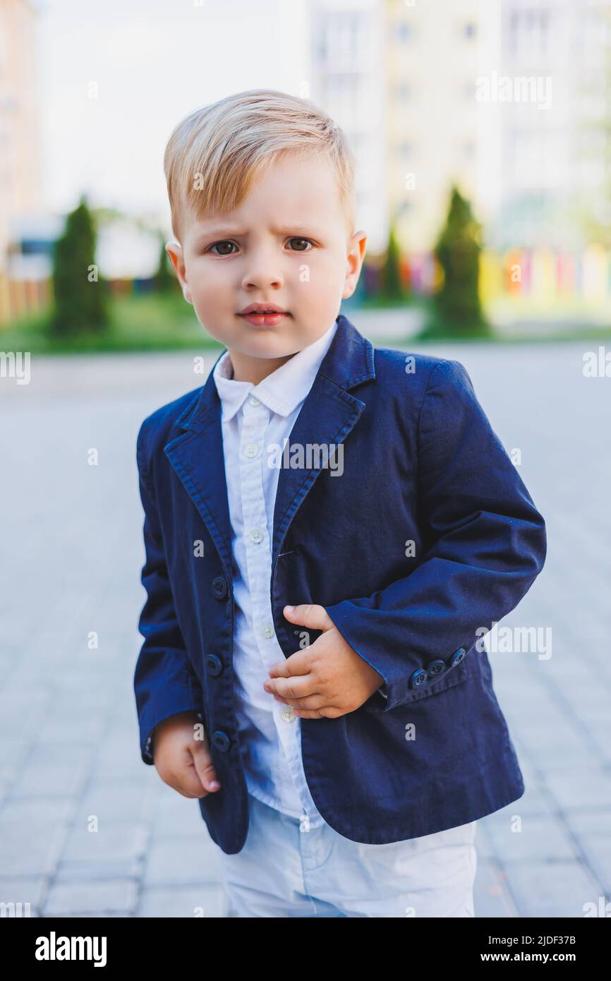 A little boy 2 years old in a shirt and jacket stands on the street