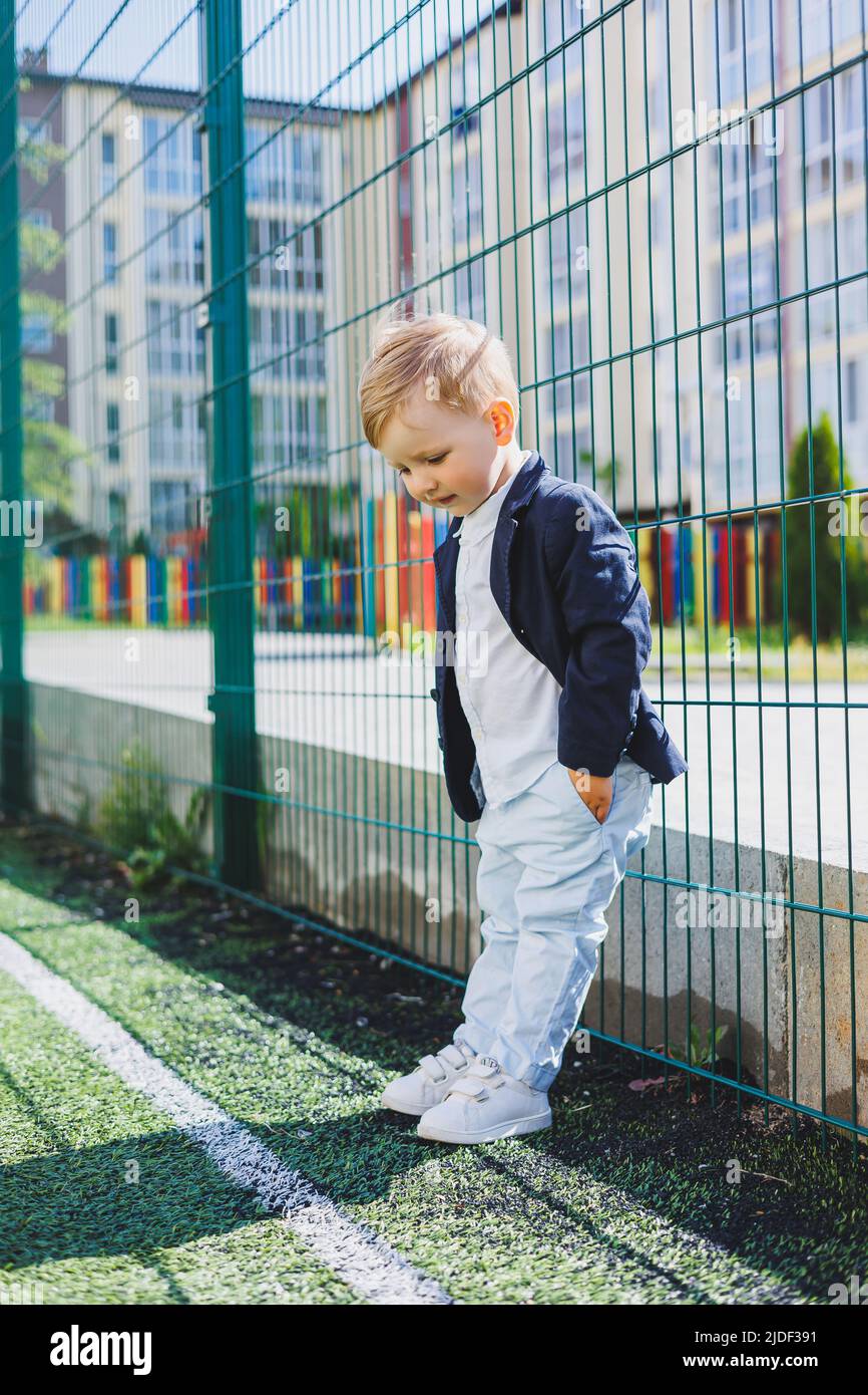 A little boy 2 years old in a shirt and jacket stands on the street