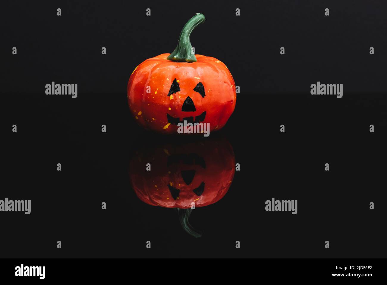 Halloween pumpkin with typical face isolated on black reflective surface. Background is dark. Stock Photo