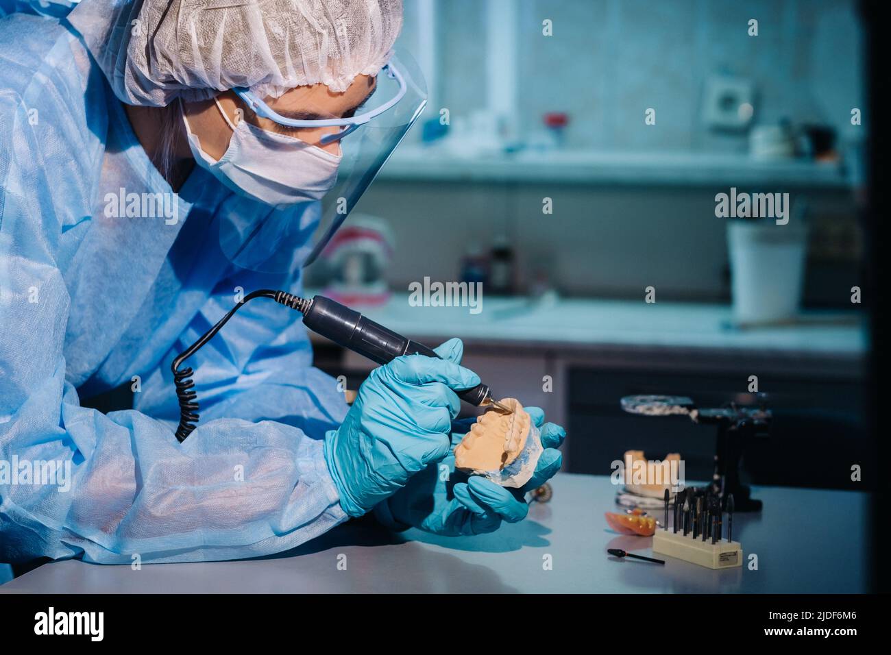 A dental technician in protective clothing is working on a prosthetic tooth in his laboratory