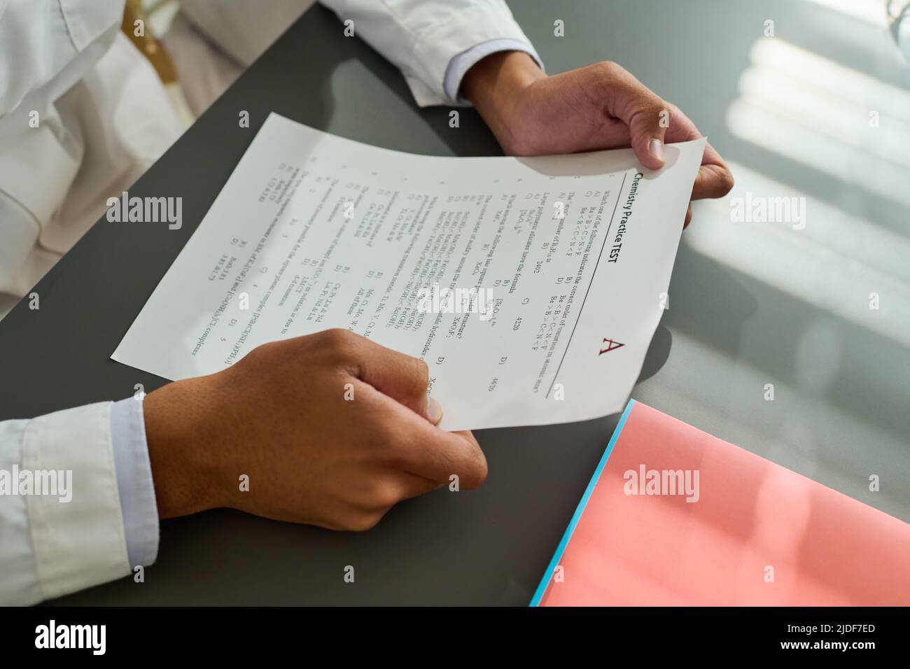 Hands of African American teenage guy holding paper with exam test and looking through assignments while sitting by desk at lesson Stock Photo