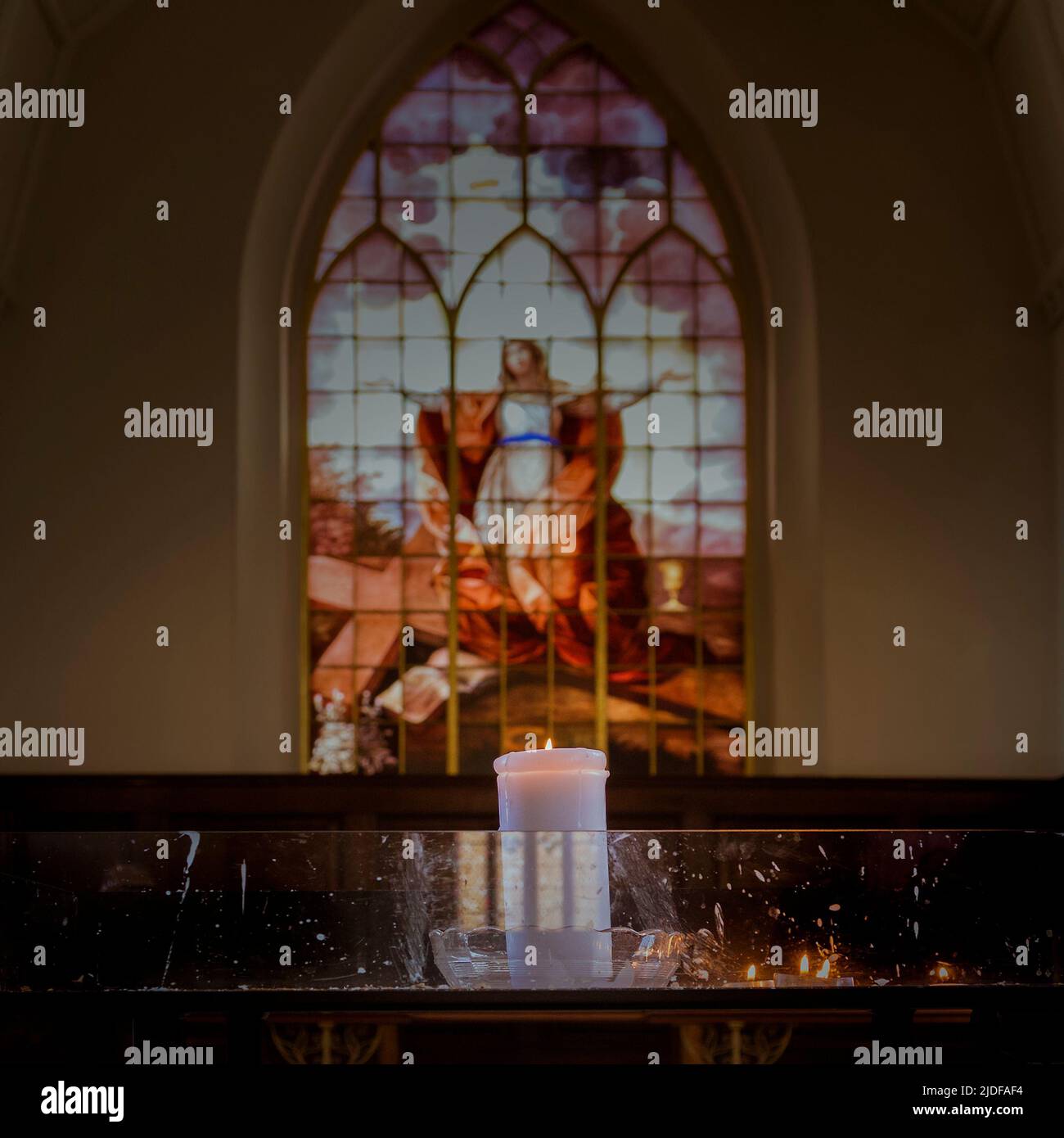 A candle burning in front of a stained glass window in a church. Hope, prayer, courage, faith, spirituality concept. Stock Photo