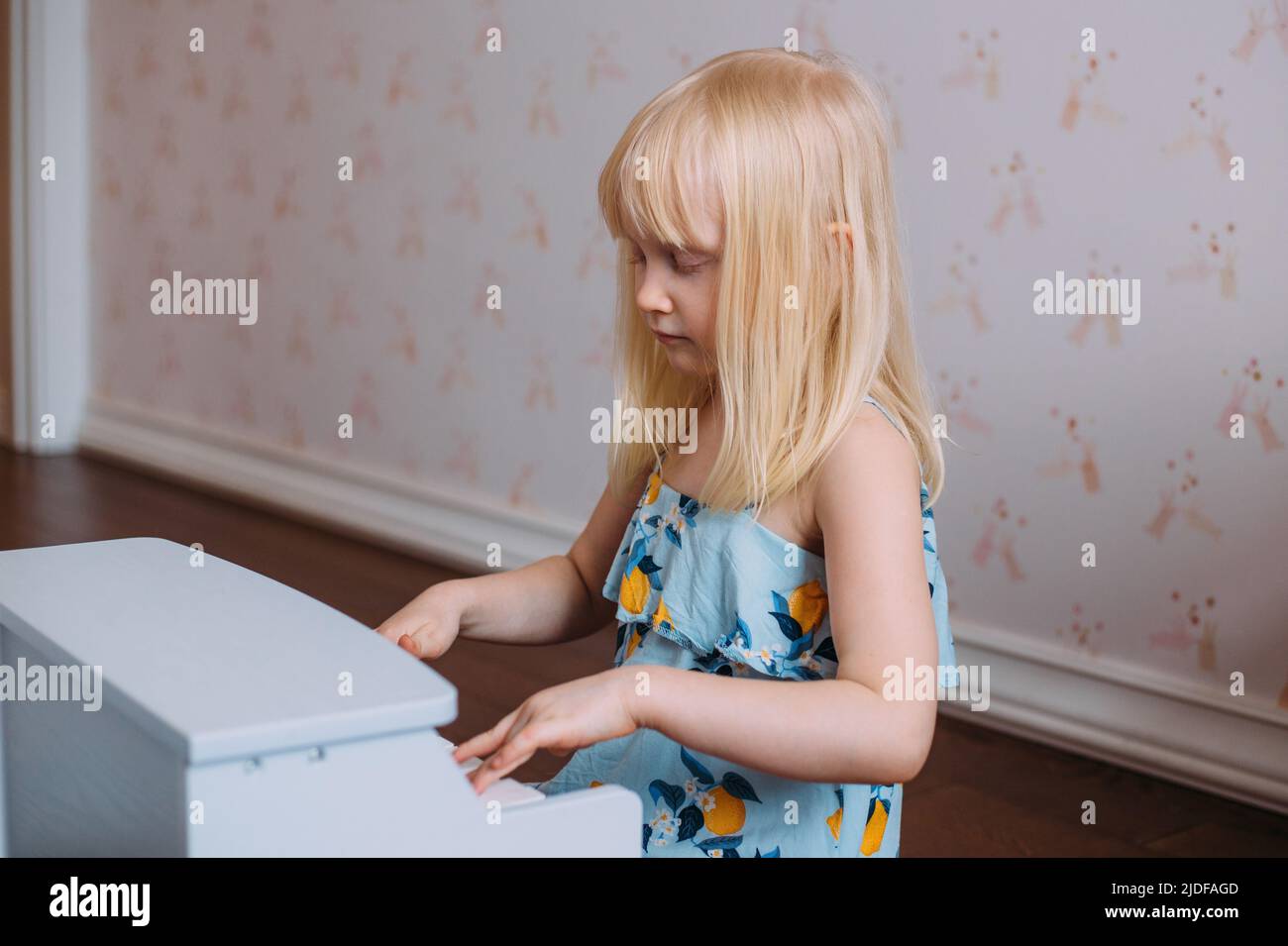 Little blonde girl plays a toy piano at home. Musical development in childhood Stock Photo