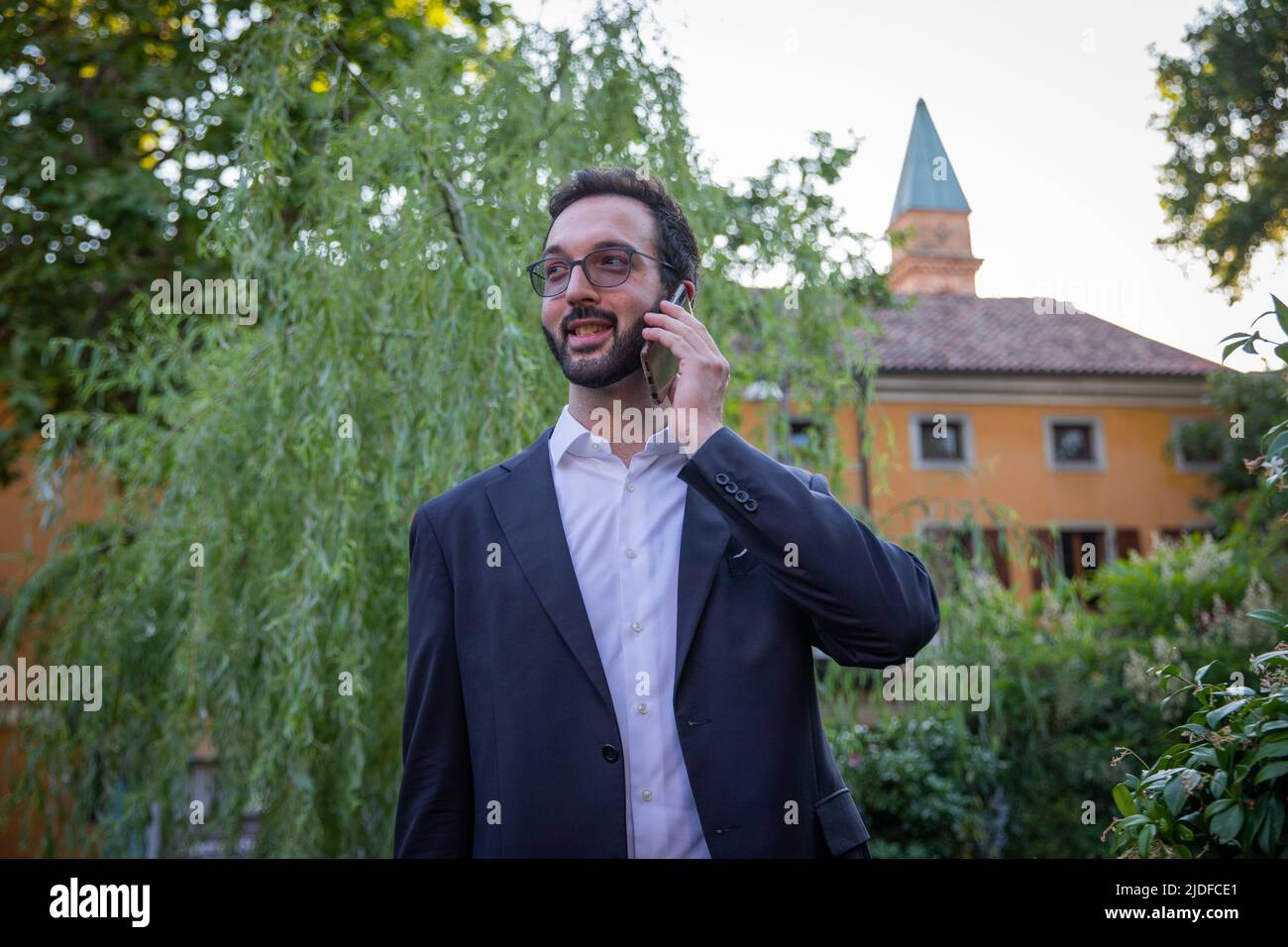 Young businessman in dark jacket and white shirt on phone with a partner. Business concept. Stock Photo