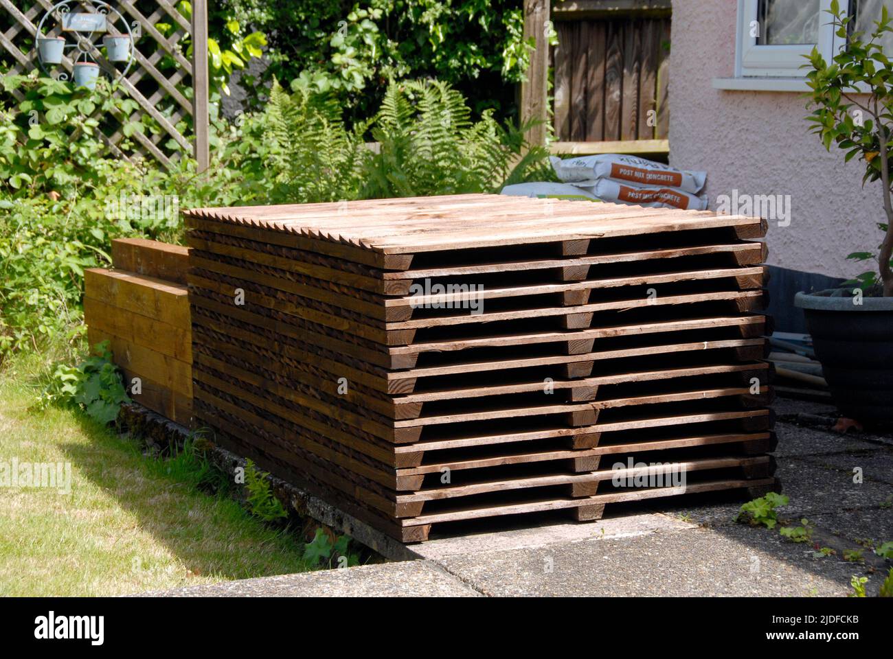 Stack of wooden fence panels, posts, gravel boards and cement mix, stored on patio ready for replacing old domestic garden fence Stock Photo