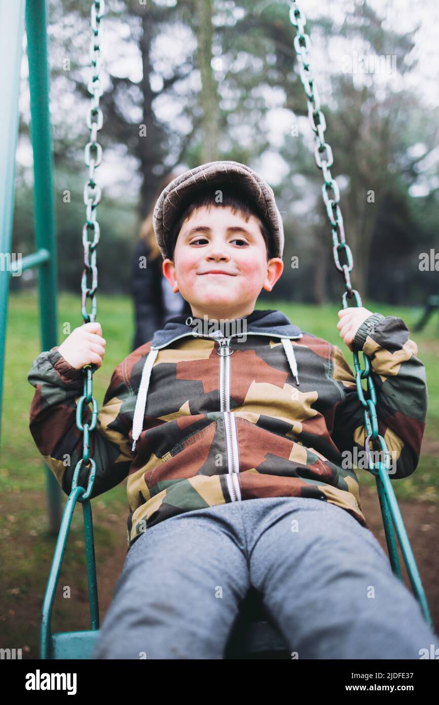 Smiling kid playing in a swing at a playground. Recreational enjoying at the park. Vertical Stock Photo