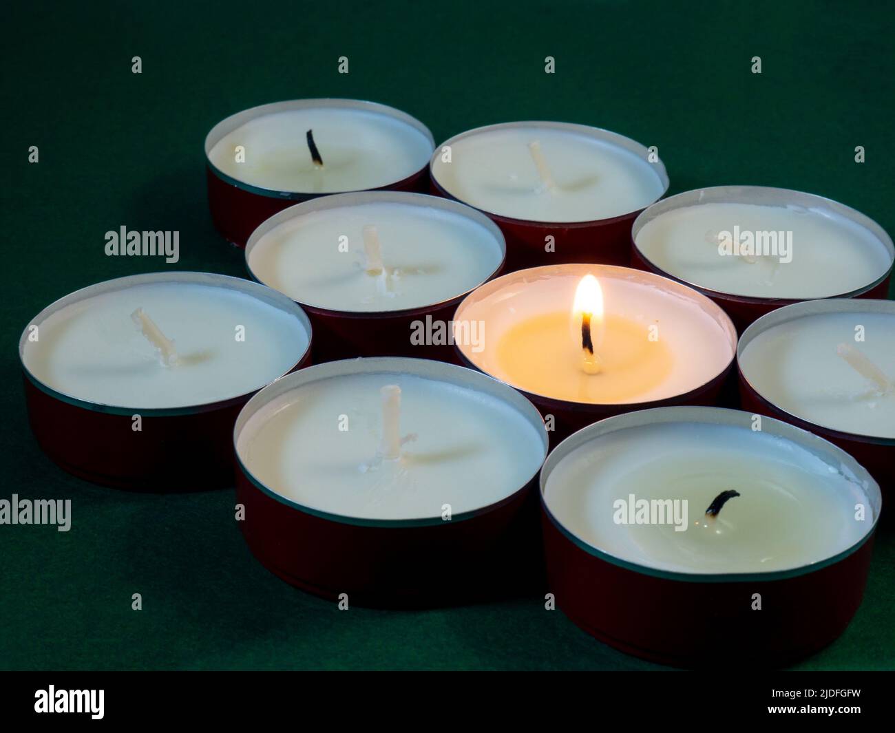 Short candles are burning on a green surface. Lots of small candles. Not all candles are lit