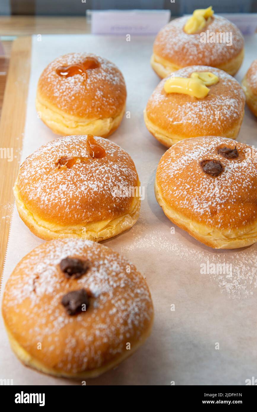 Different flavour donuts, sprinkled with powdered sugar, displayed in a bakery Stock Photo
