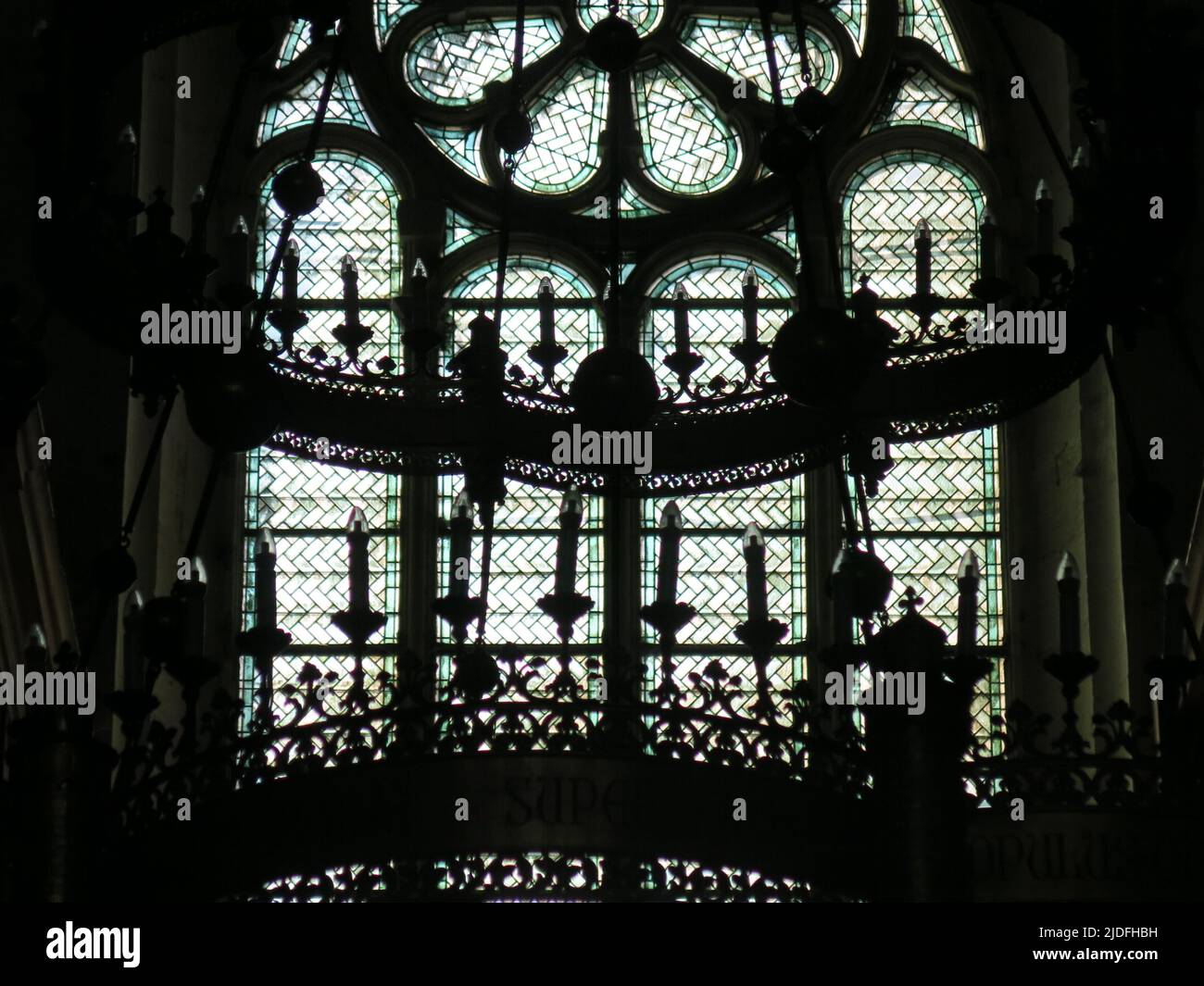 Abstract, black & white close-up of the ornate candelabra silhouetted against the stained glass windows of the Cathedral Saint Vincent in Viviers. Stock Photo