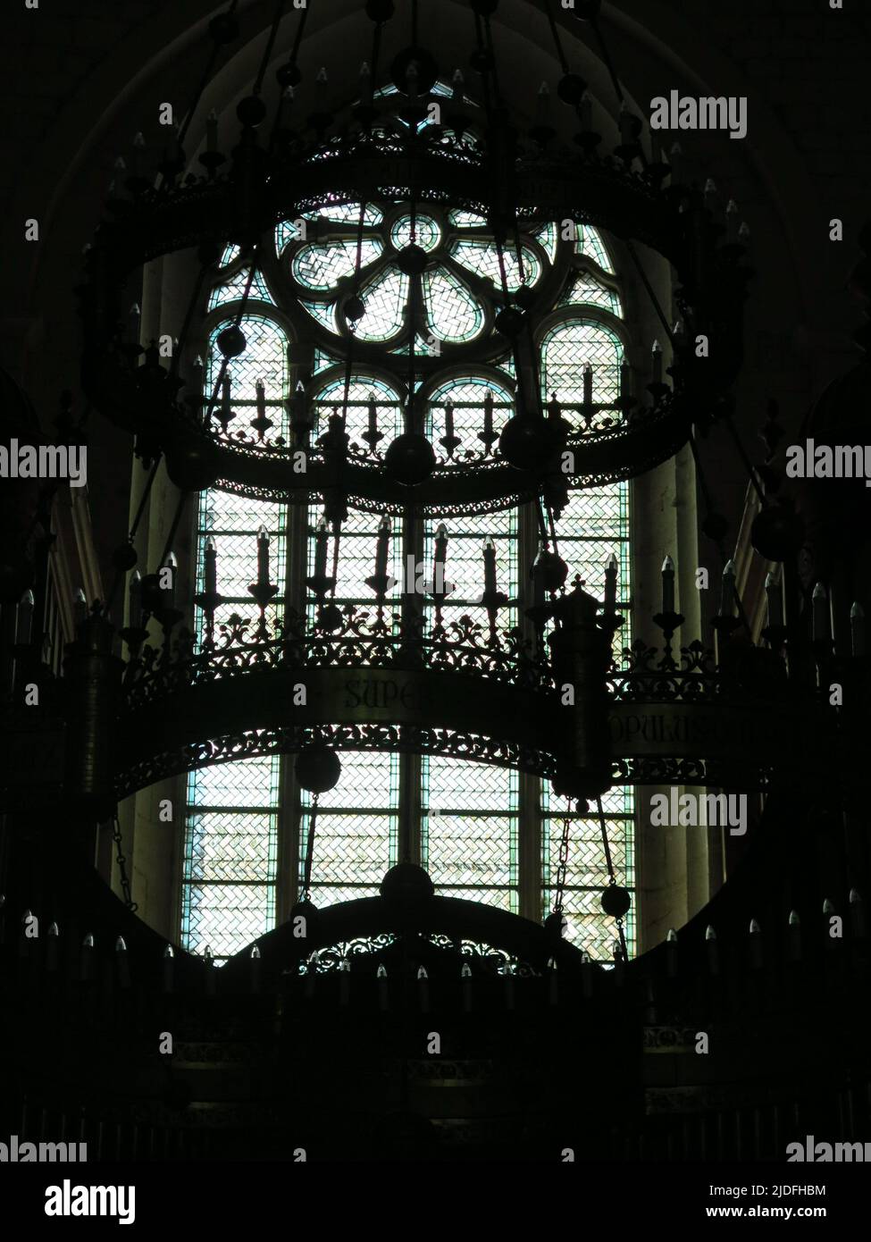 Abstract, black & white close-up of the ornate candelabra silhouetted against the stained glass windows of the Cathedral Saint Vincent in Viviers. Stock Photo