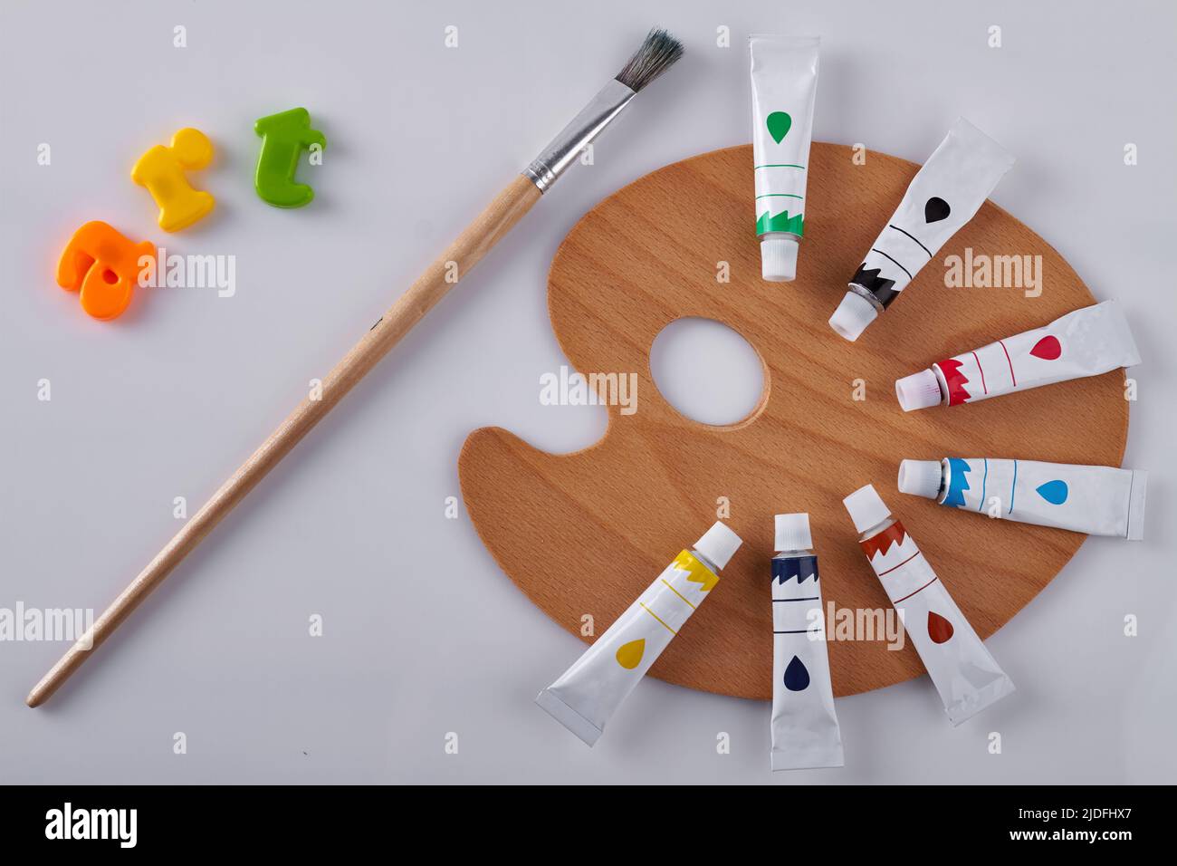 Clean wooden palette with paint brush on white background. Oil tubes in