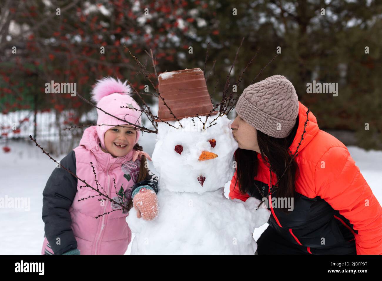 Smiling little girl with missing front tooth and woman kissing snowman