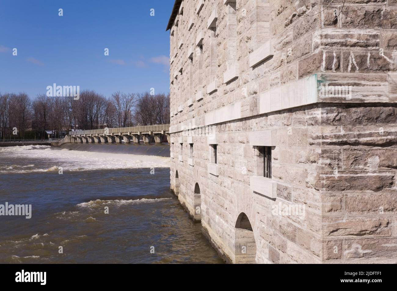 New Mill building and water flow control dam on Riviere des Mille-Iles river in spring, Old Terrebonne, Lanaudiere, Quebec, Canada. Stock Photo