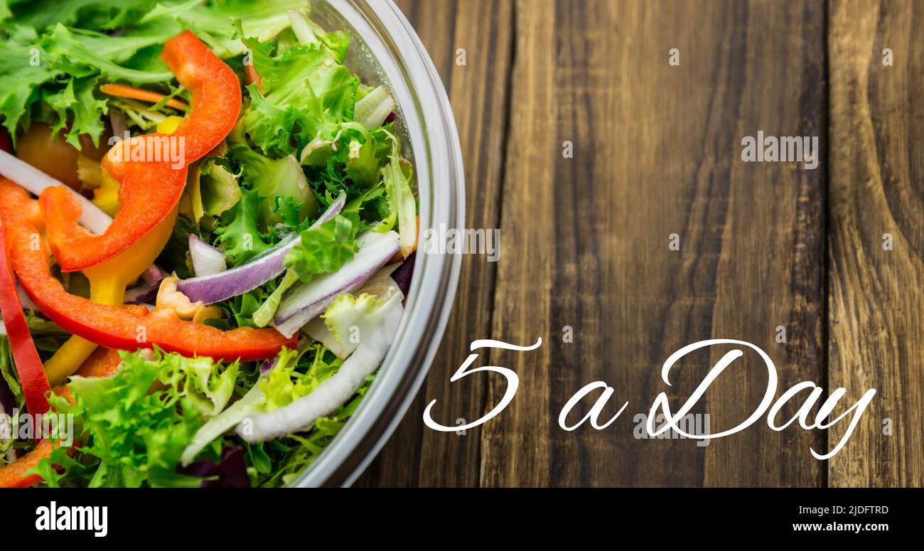 Image of 5 a day day text in white, over bowl of fresh salad on wooden boards Stock Photo