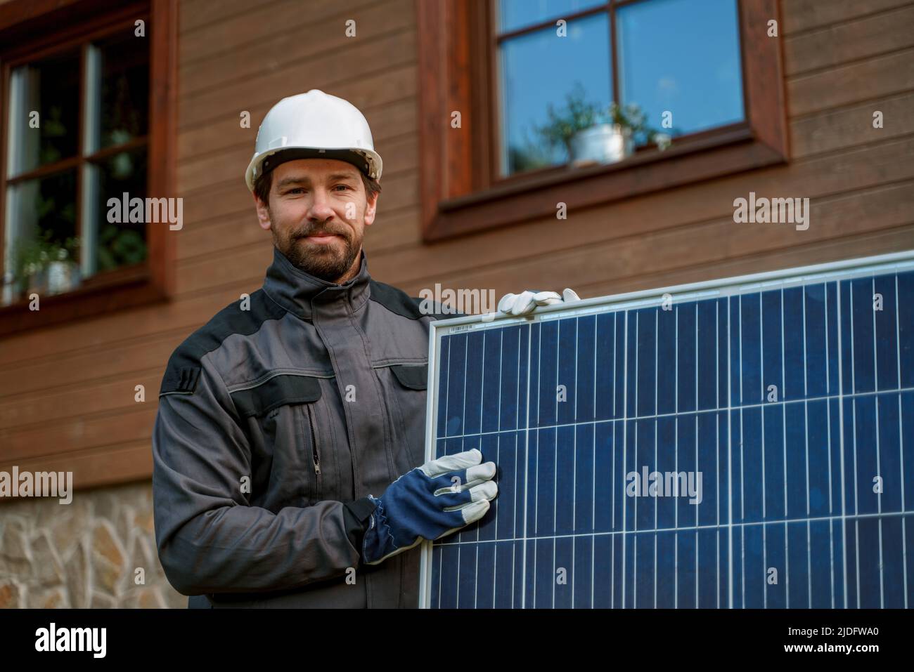 Smiling handyman solar installer carrying solar module while installing solar panel system on house. Stock Photo