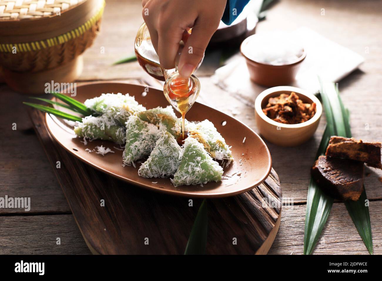 Pour Palm Sugar on Lupis, Indonesian Traditional Snack Made From Sticky Rice, Wrapped with Banana Leaf, Shape Triangle  Served with Liquid Palm Sugar Stock Photo