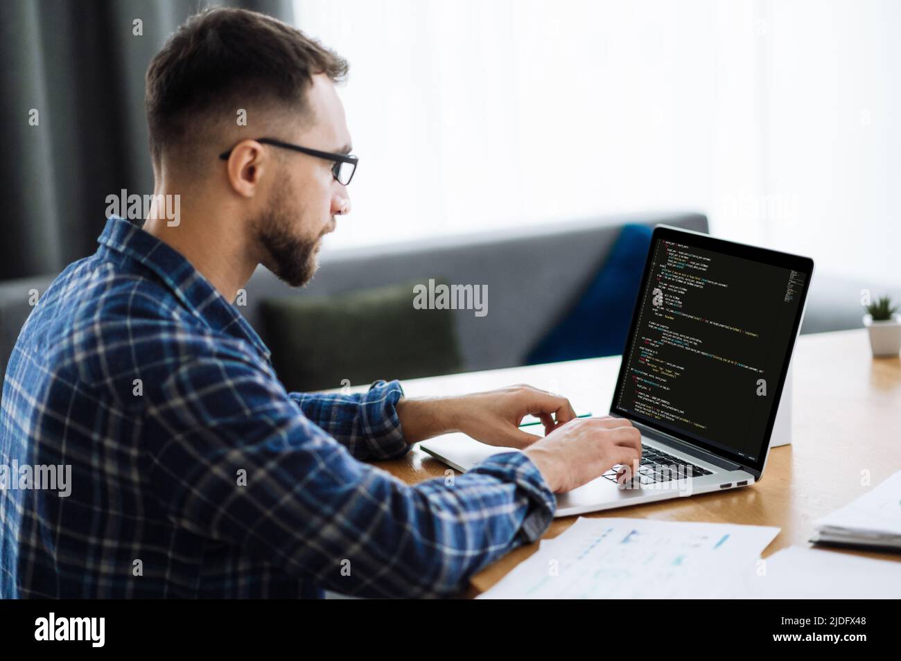 Developing coding technologies, IT concept. Side view at male IT-specialist uses laptop with programming code on the screen. Smart male programmer working at home with coding technology, writing codes Stock Photo