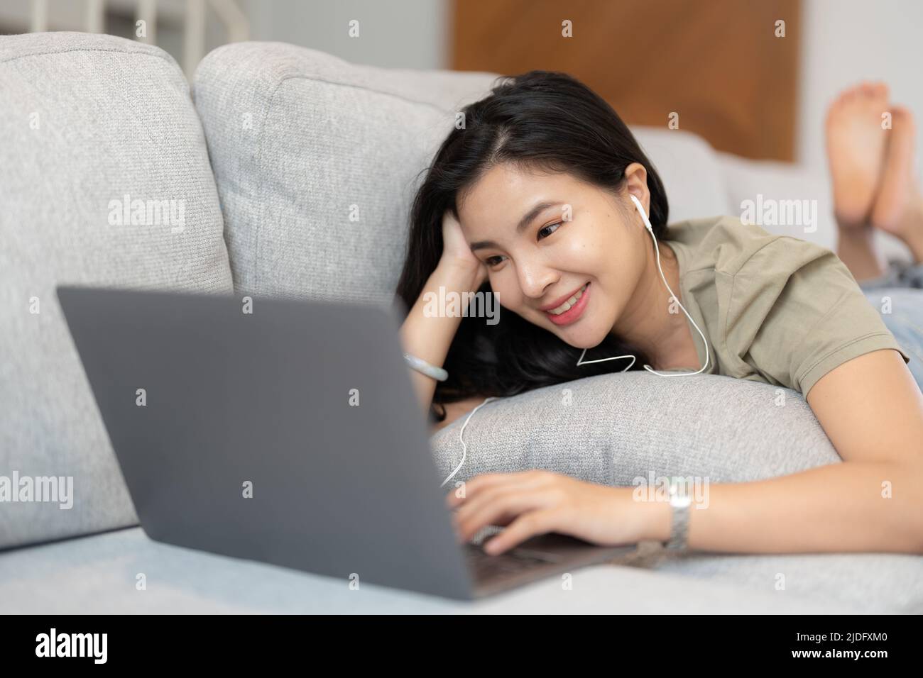 Relaxed woman using laptop in living room, enjoying working, internet shopping, checking social network, reading news or communicating online with Stock Photo