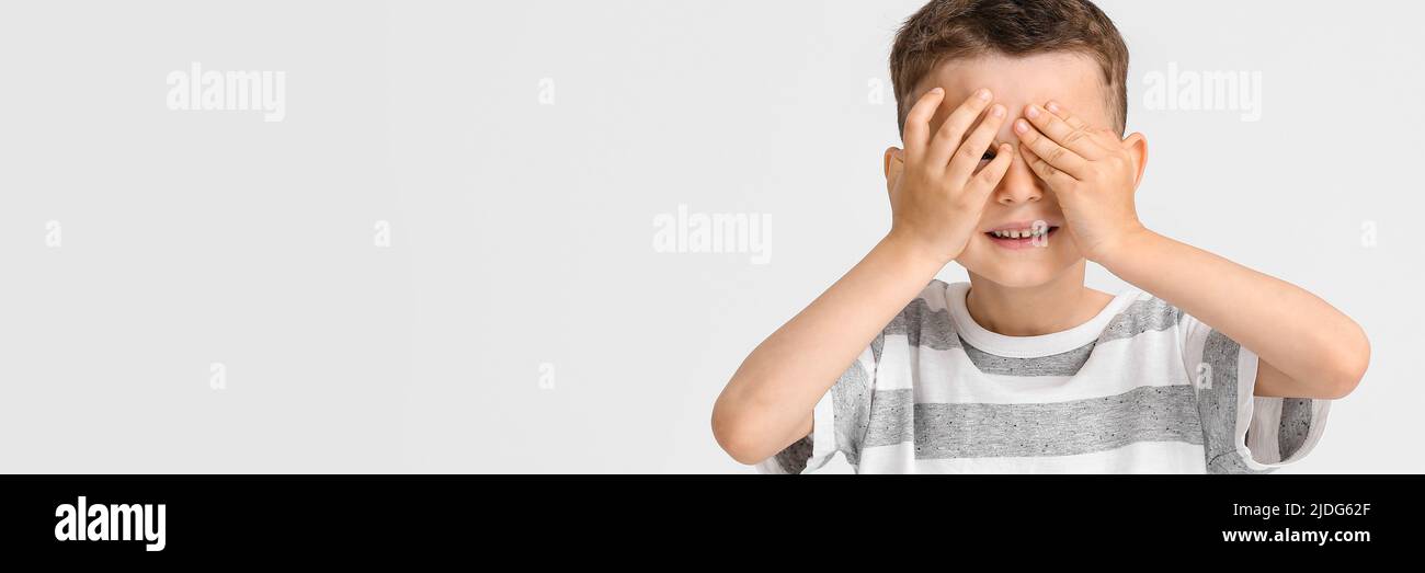 Portrait of cute little boy covering eyes with hands on light ...