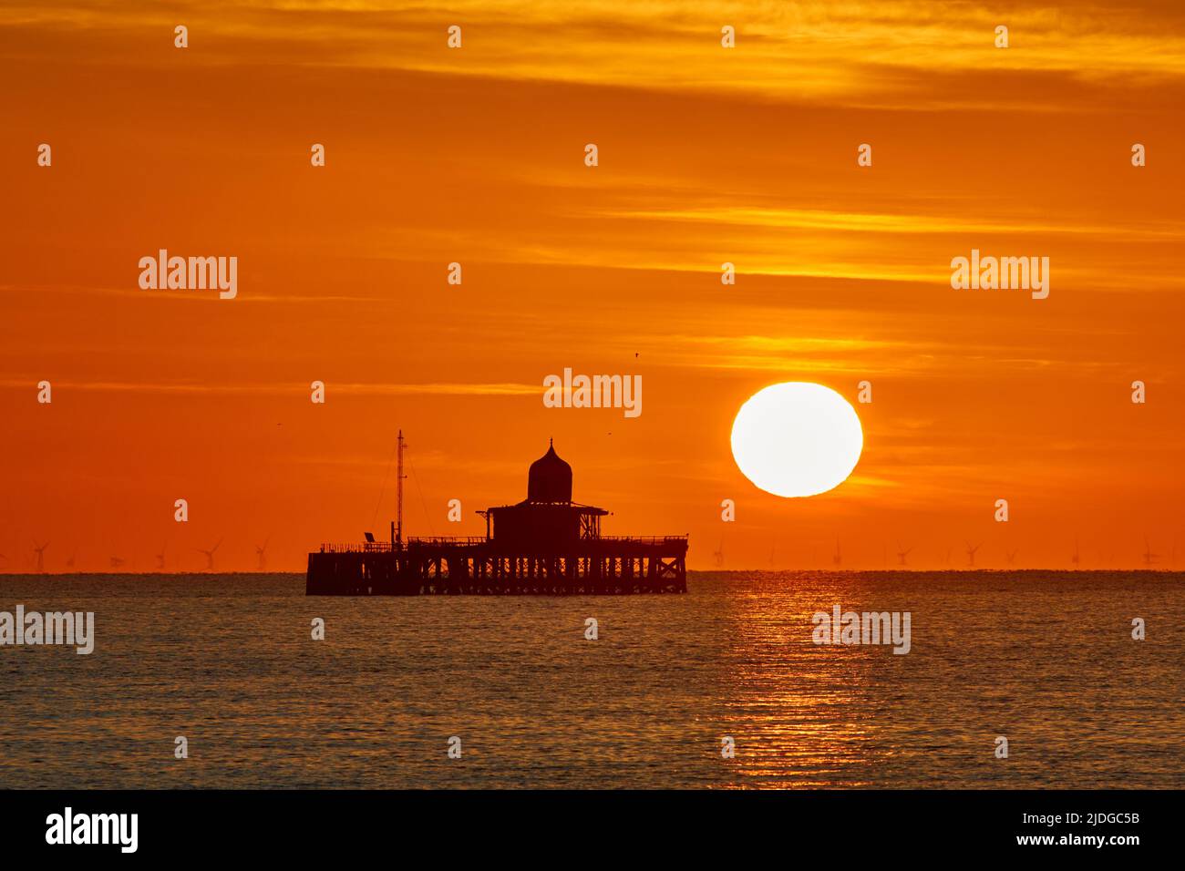 Herne Bay, Kent, UK. 21st June 2022: UK Weather. Sunrise on the summer solstice at Herne Bay in Kent, with the old pier head silhouetted against the morning orange glow as another bright sunny and warm day starts. Credit: Alan Payton/Alamy Live News Stock Photo