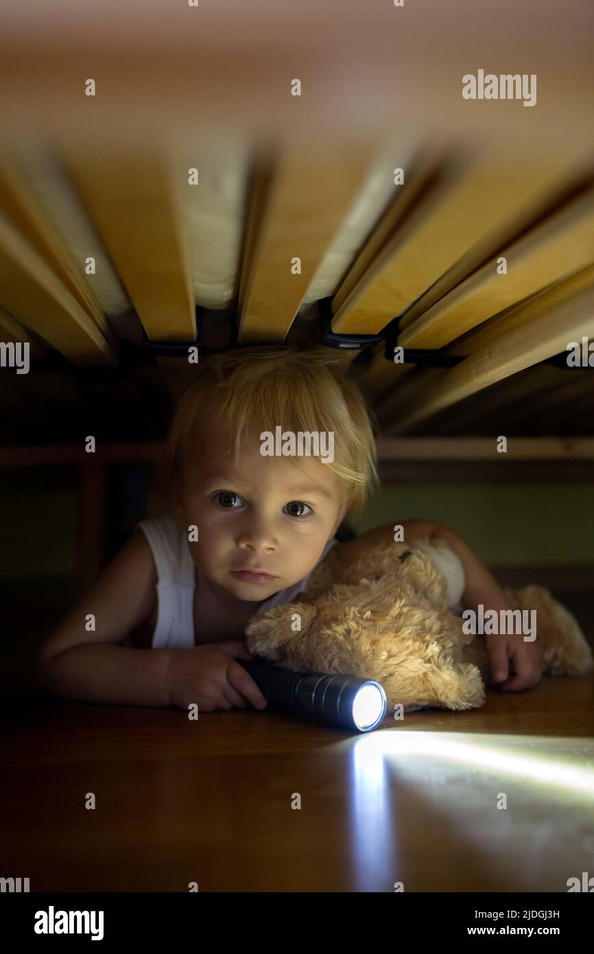 Little child, hiding under the bed, hugging teddy bear and holding