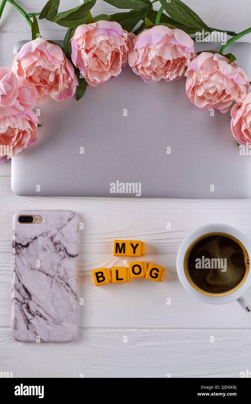 Cup of coffee with laptop and flowers on white desk. My blog concept. Smartphone with marble case. Stock Photo
