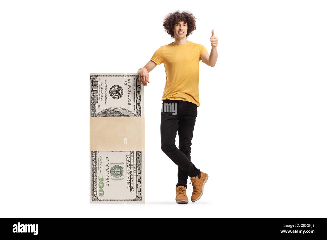Young man leaning on a stack of money and showing thumbs up isolated on white background Stock Photo
