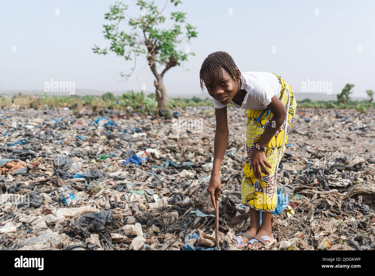 Innocent little African girl who collects recyclable waste in a landfill smiling at the camera not aware of being exploited; child labour concept Stock Photo