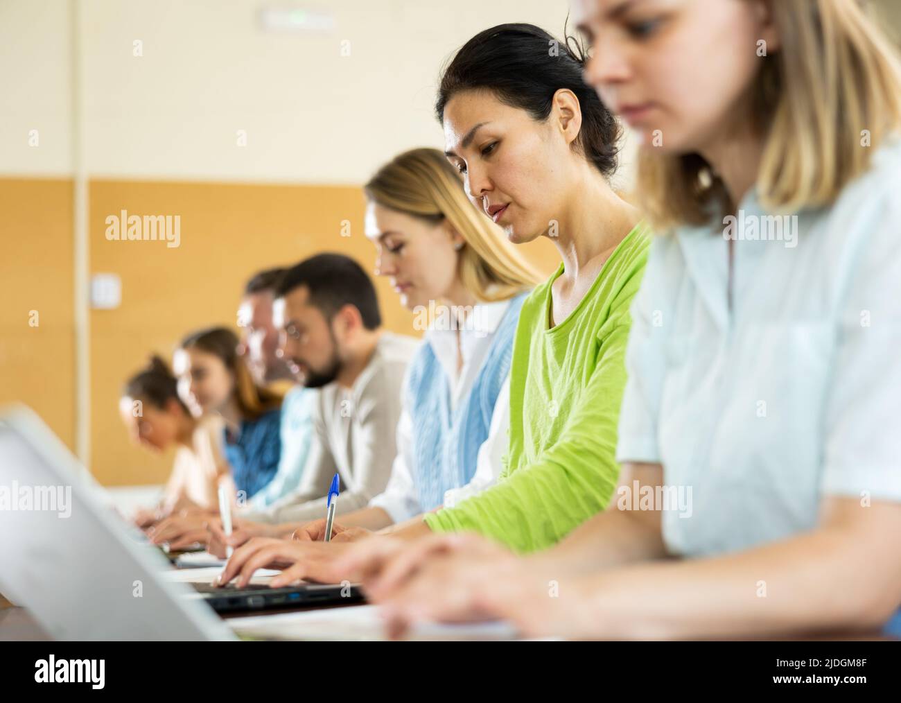 Woman university student sitting at table and handwriting, using laptop ...