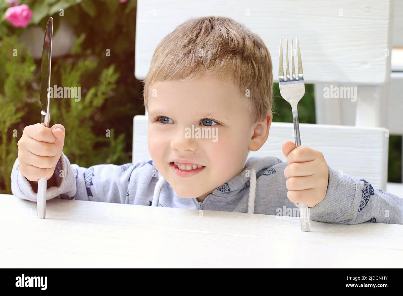 The smiling child shows that he wants to eat. Kid holding fork and