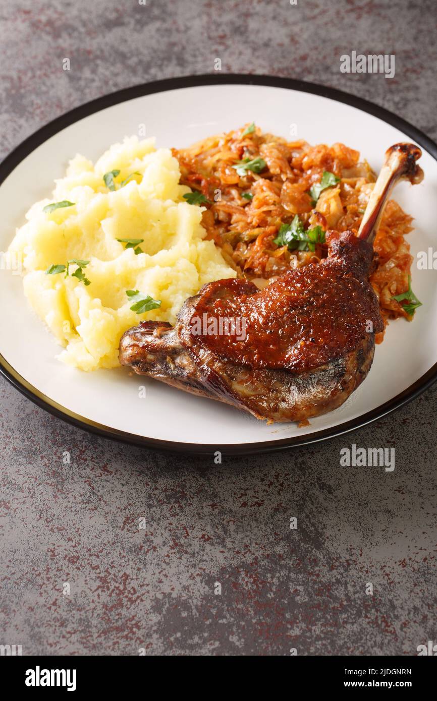 Baked duck leg serving with mashed potatoes and stewed cabbage close-up in a plate on the table. Vertical Stock Photo