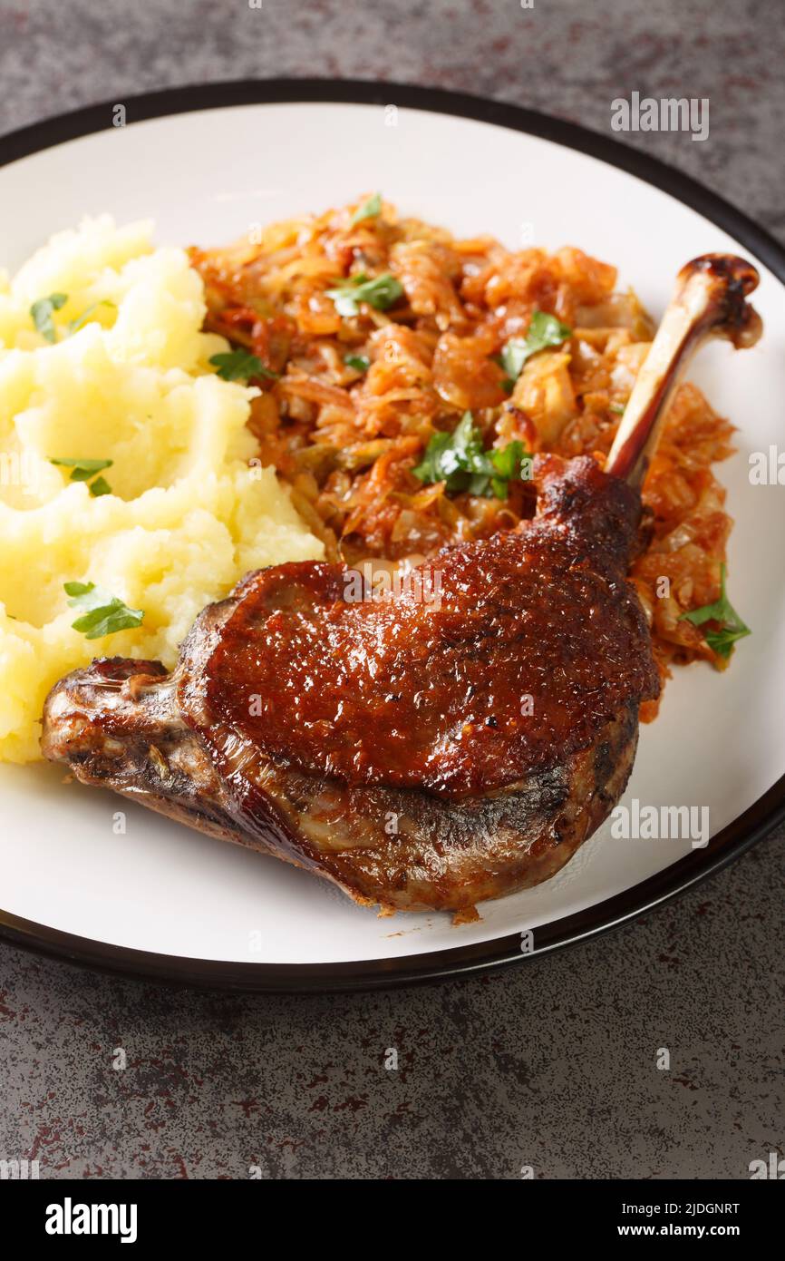 Romanian Rata pe varza duck leg serving with mashed potatoes and stewed cabbage close-up in a plate on the table. Vertical Stock Photo