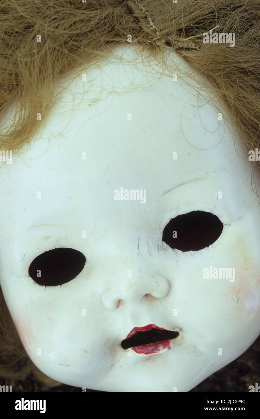 Close up of white face of 1950s doll with black holes where her eyes should be and open mouth and untidy hair Stock Photo