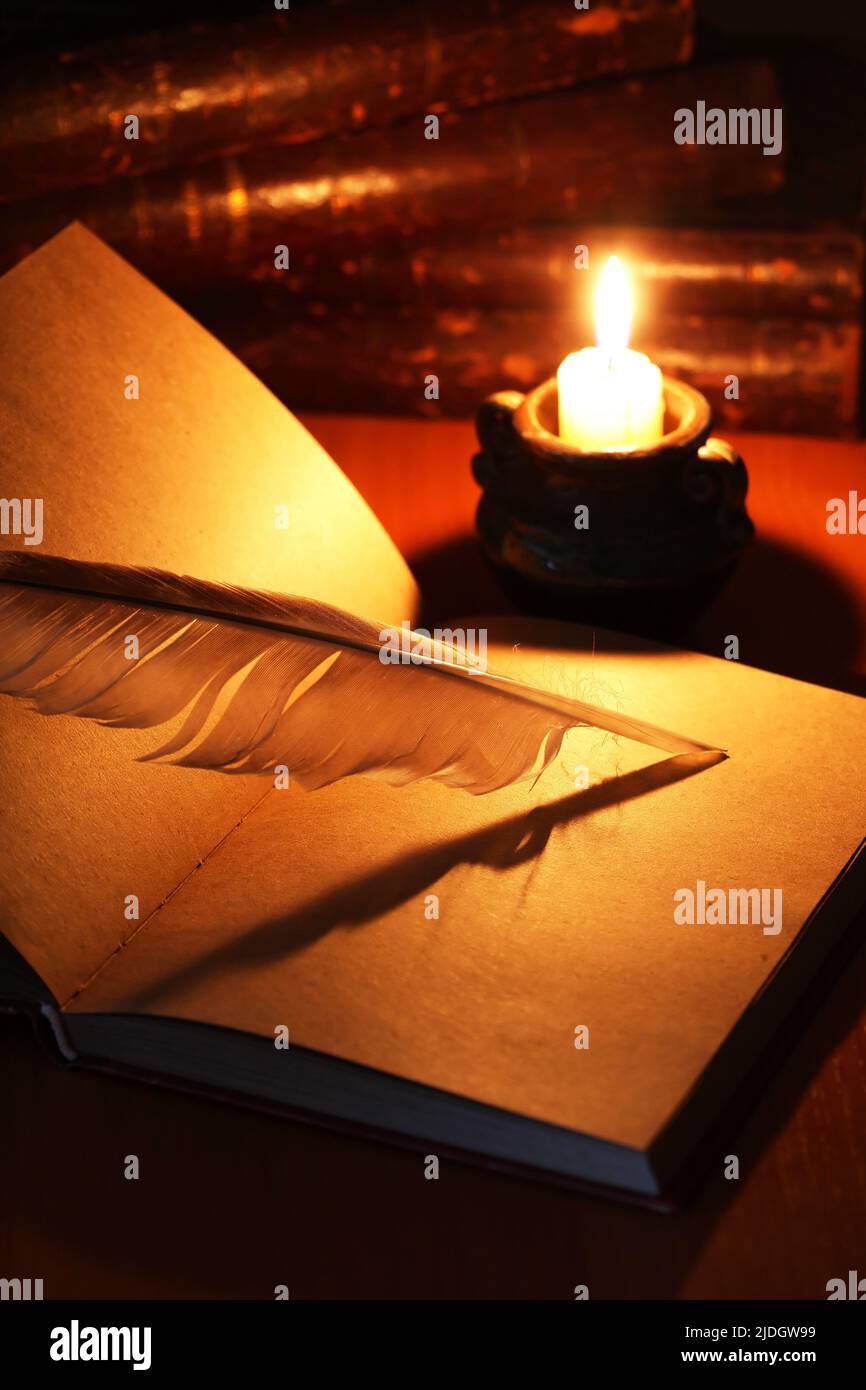 Vintage still life with open book and quill pen near lighting candle Stock Photo