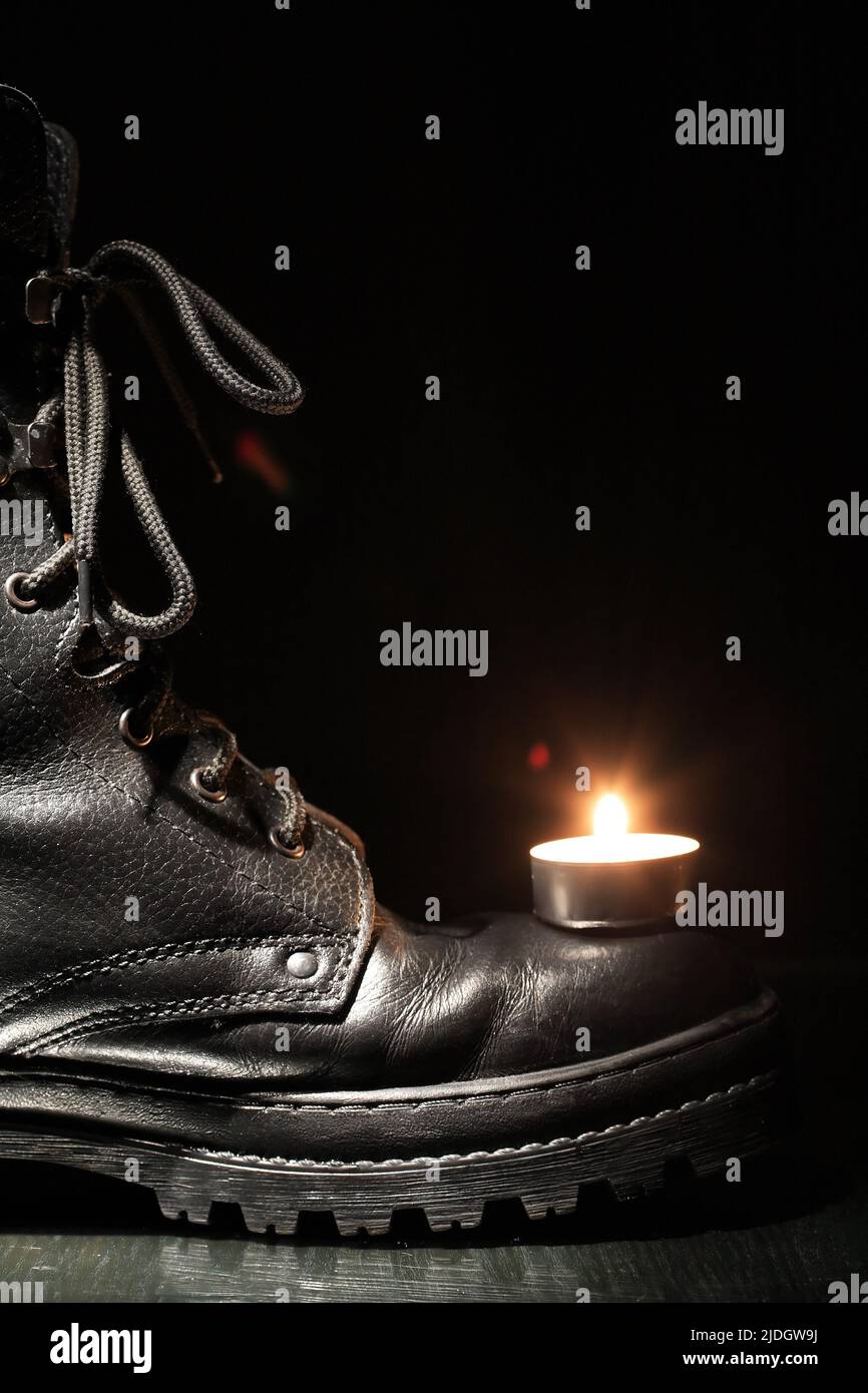 Lighting candle on black military boot against dark background Stock Photo