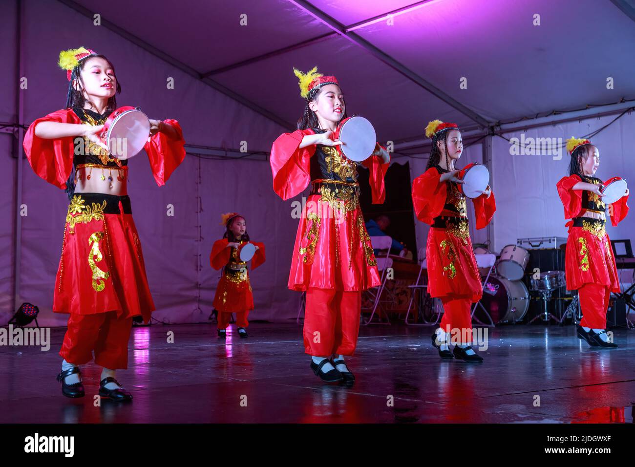 Young Asian girls in colorful folk costumes dancing on stage with tambourines during Moon Festival celebrations. Auckland, New Zealand Stock Photo
