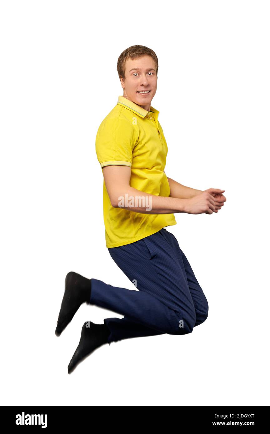 Funny attractive guy in yellow Tshirt, blue pants and black socks jumping isolated on white
