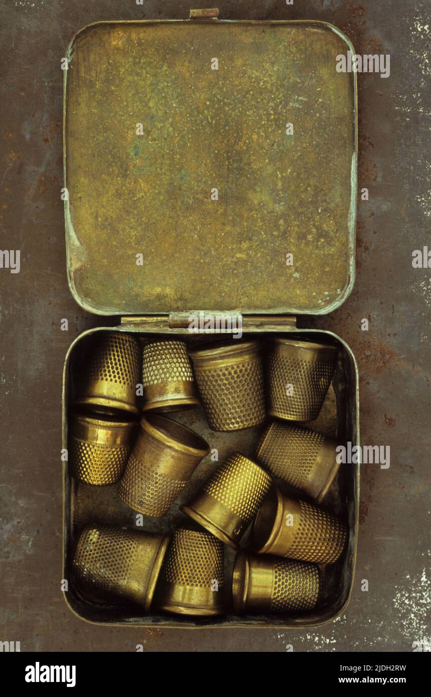 Collection of antique brass thimbles in brass tin on rusty metal sheet