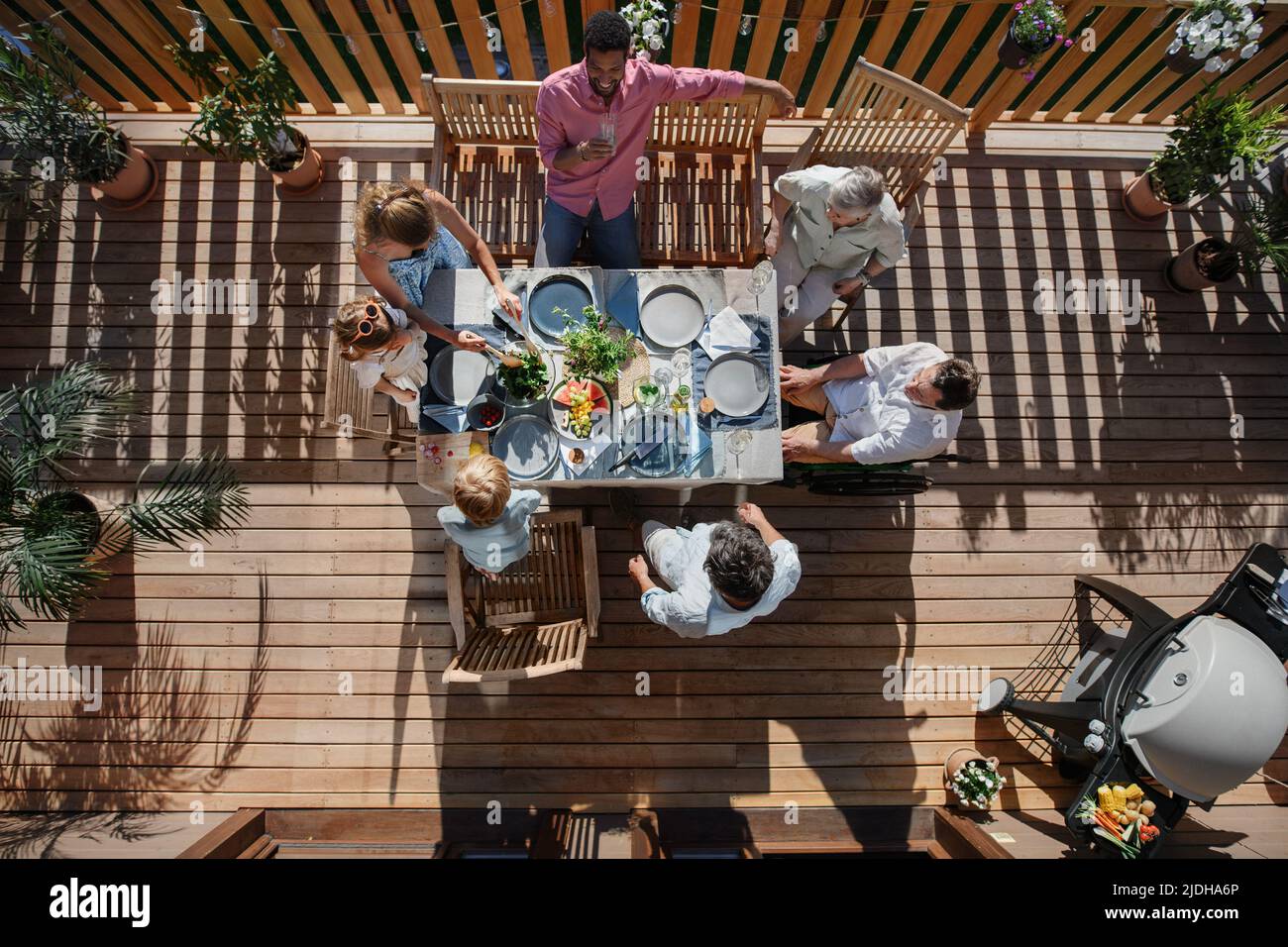 Top view of 3 generations family eating at barbecue party dinner on patio, people sitting at table on patio with grill. Stock Photo